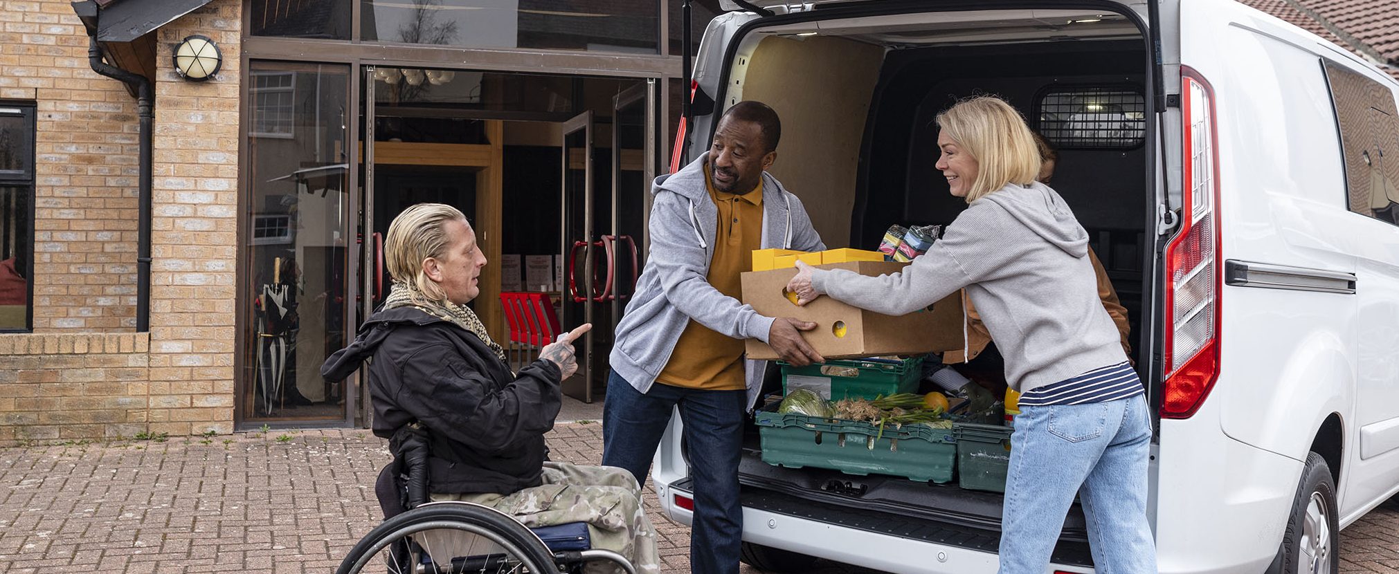 A man and woman load boxes into a van and chat with a man in a wheelchair.