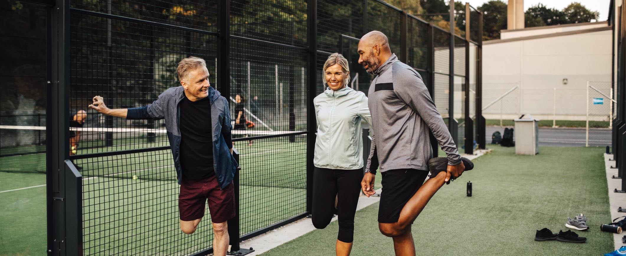 Standing outside a tennis court, three friends smile and stretch their legs.