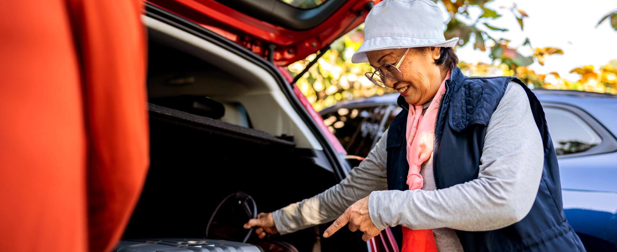 A woman smiles while loading a bag into the trunk of her car.