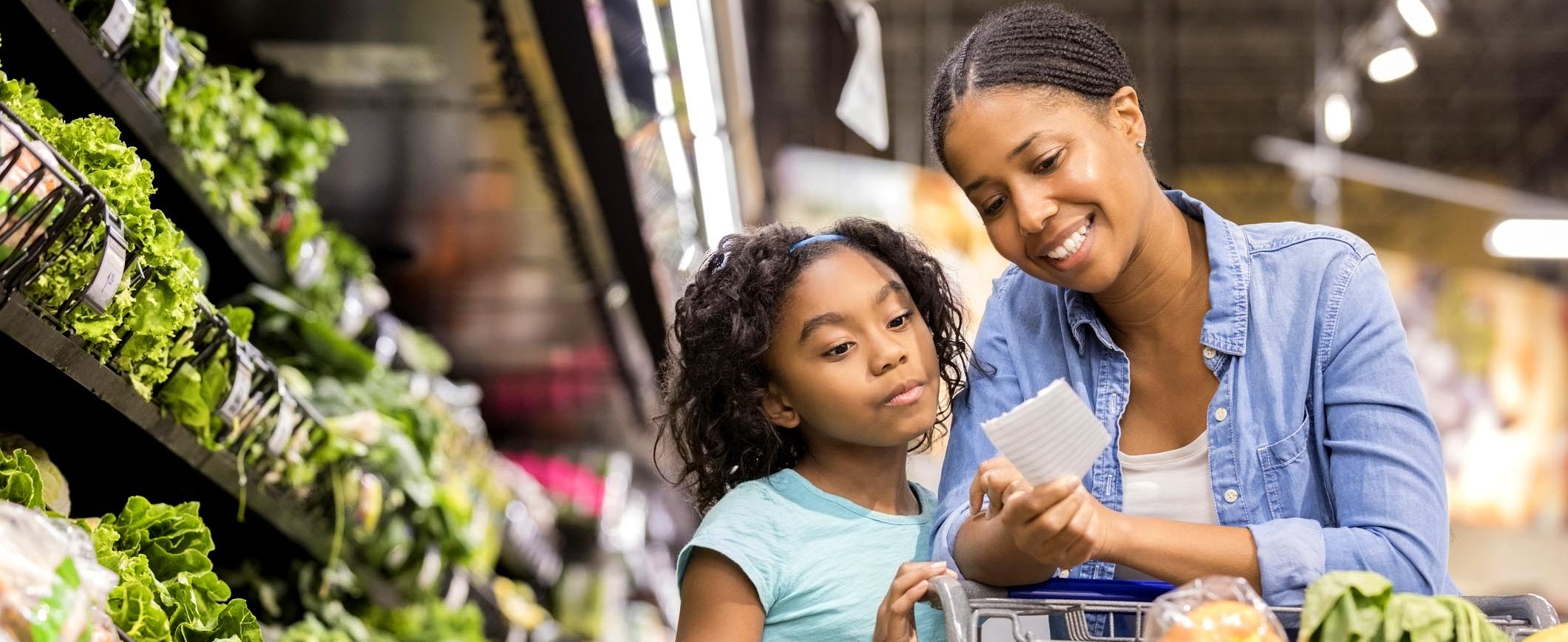 A woman and her daughter look over a shopping list in a grocery store.