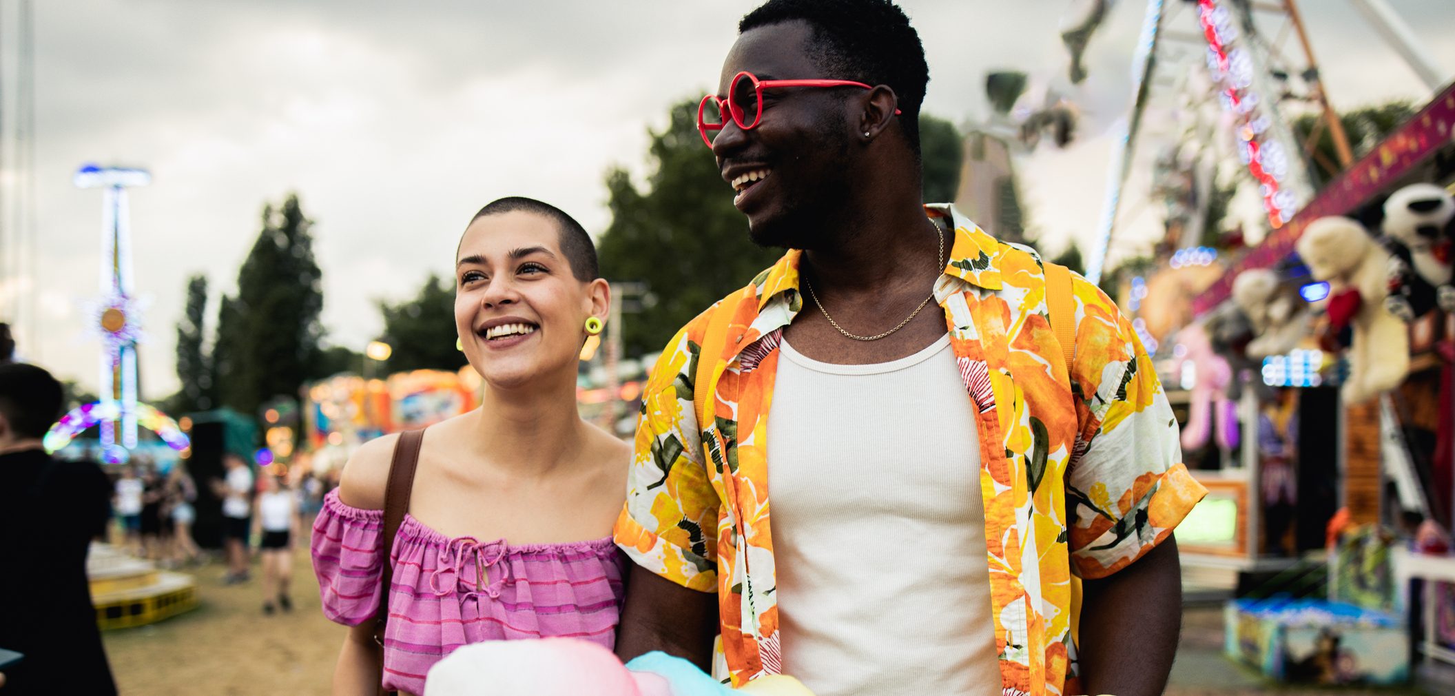 A man and woman smile as they walk through a fairground.