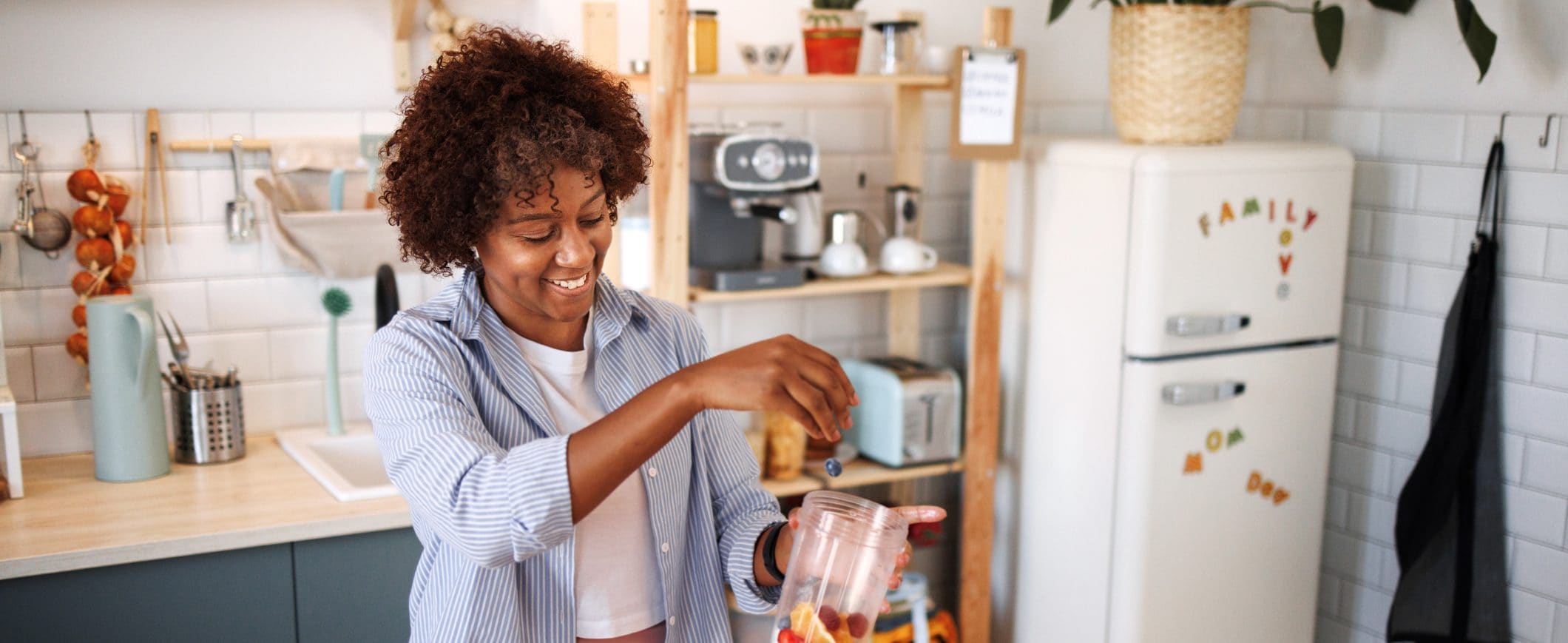 A woman stands in her kitchen and adds fruit to a jar.