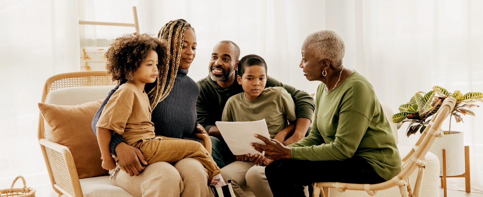 A woman holds a document while talking to a family seated across from her on a couch.