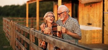 Older couple drinks coffee outside a barn.