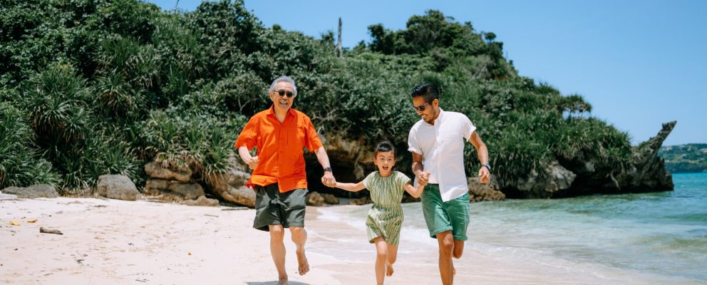 A family runs hand-in-hand along a beach on a sunny day.