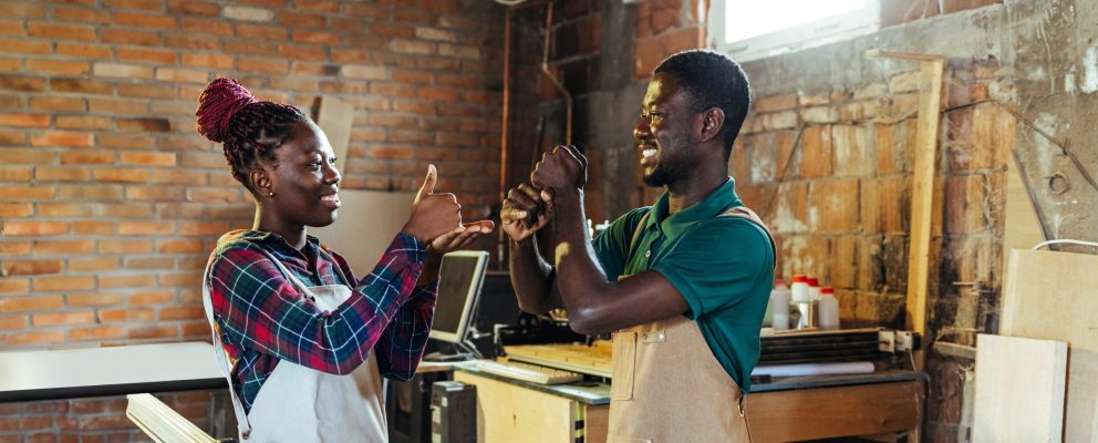 A man and woman use sign language in their workshop.