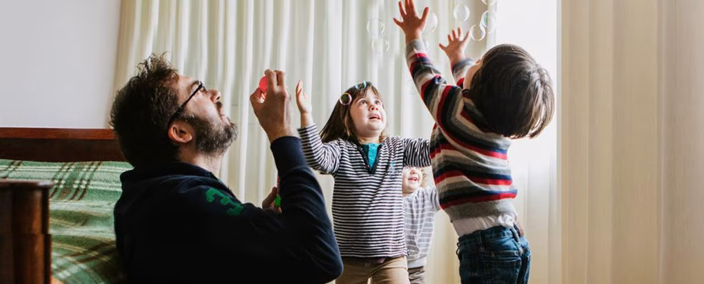 A dad blows bubbles while playing with his 2 kids