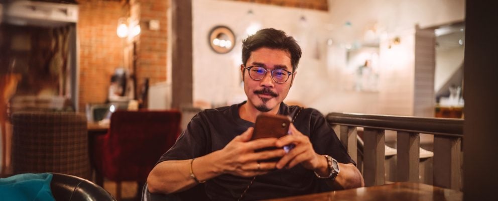 A young man sits and looks at his phone.