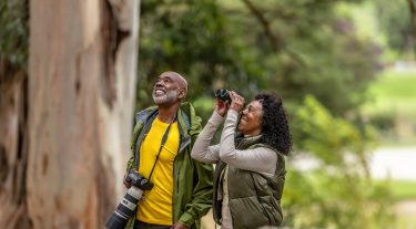 A retired couple watches birds in the woods.