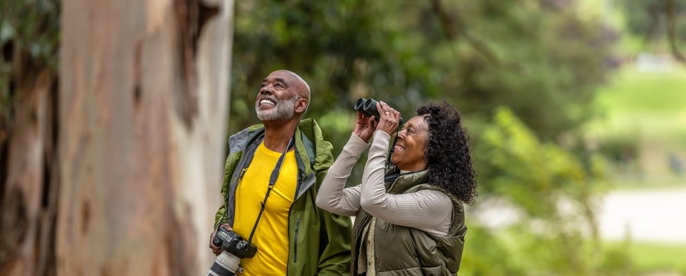 A retired couple watches birds in the woods.