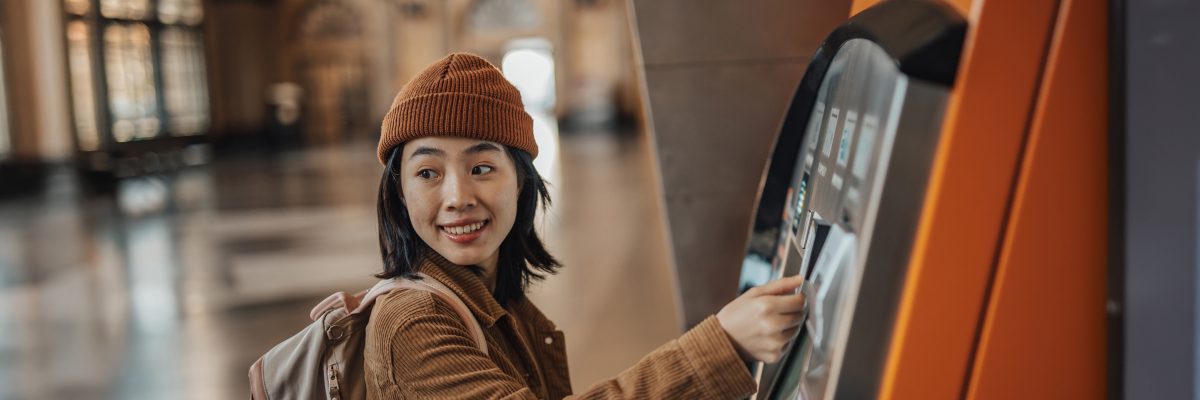 A young woman wearing a backpack uses an ATM.