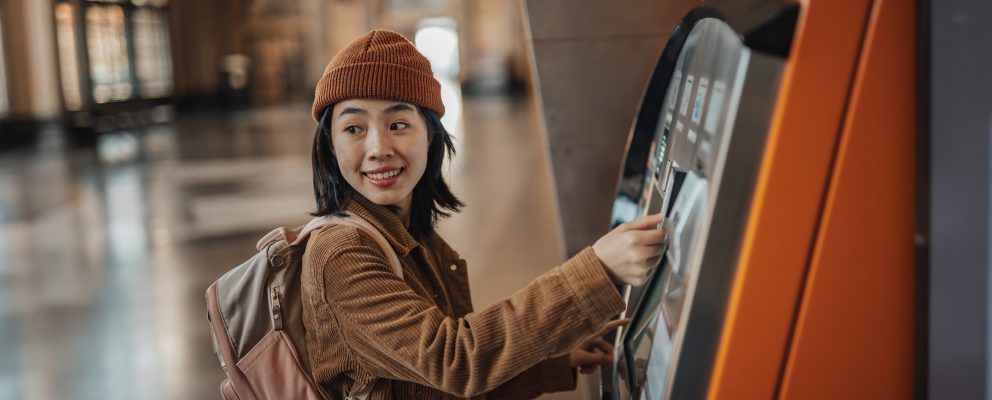A young woman wearing a backpack uses an ATM.