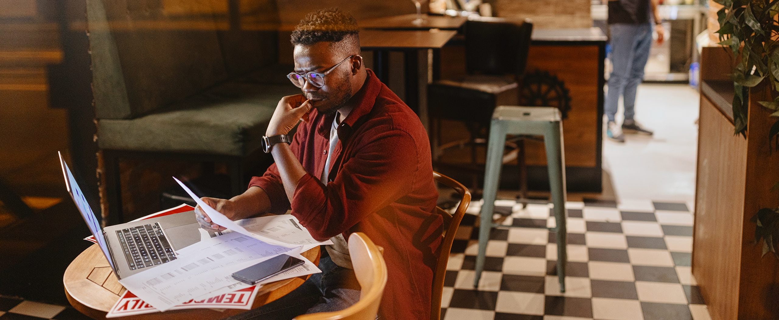 A man reviews documents beside his laptop at a café