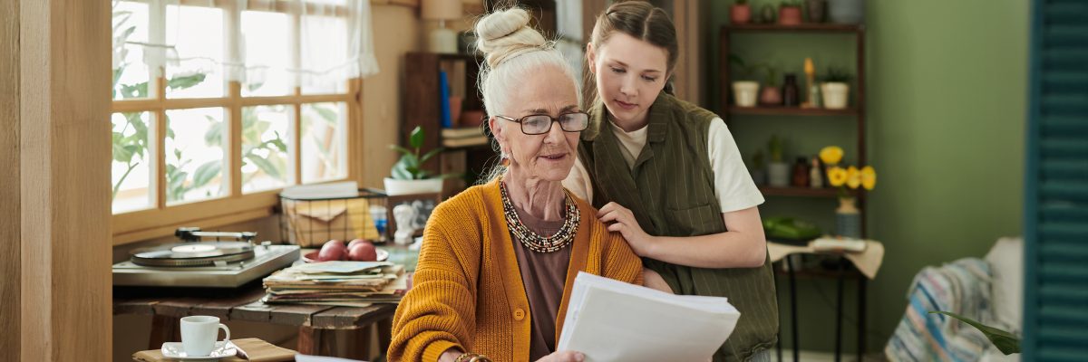 A woman and her granddaughter review documents together at a dining table.