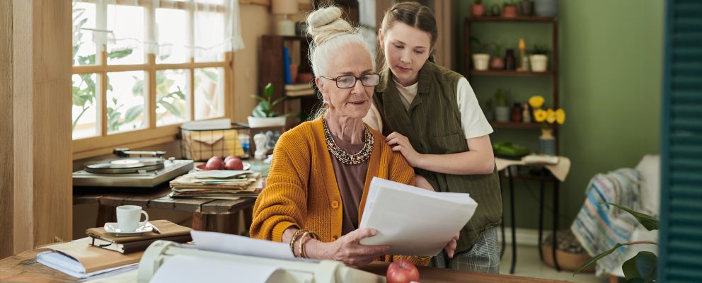 A woman and her granddaughter review documents together at a dining table.