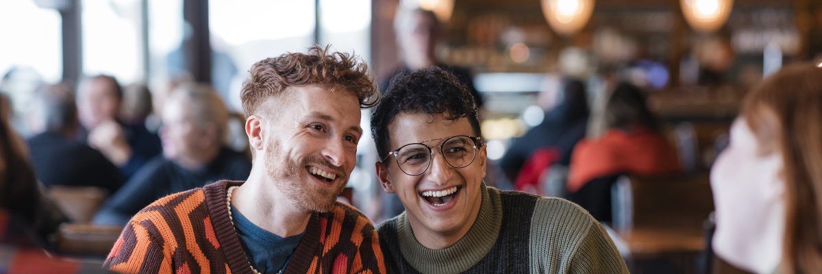 Two young men chat with friends in a crowded café.