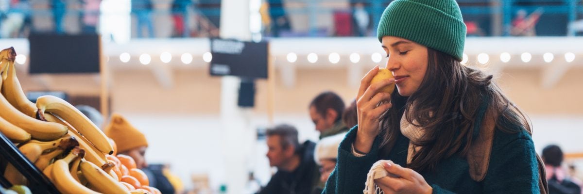 A young woman sniffing a piece of fruit at a grocery store.