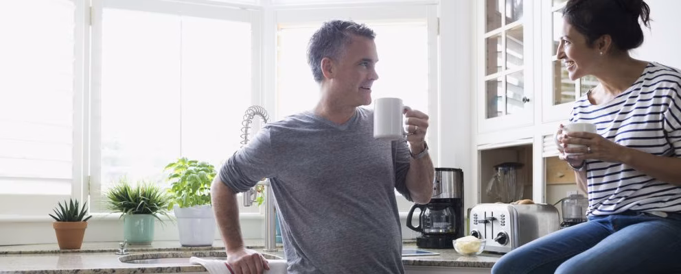 Husband and wife talking in their kitchen while enjoying a cup of coffee.