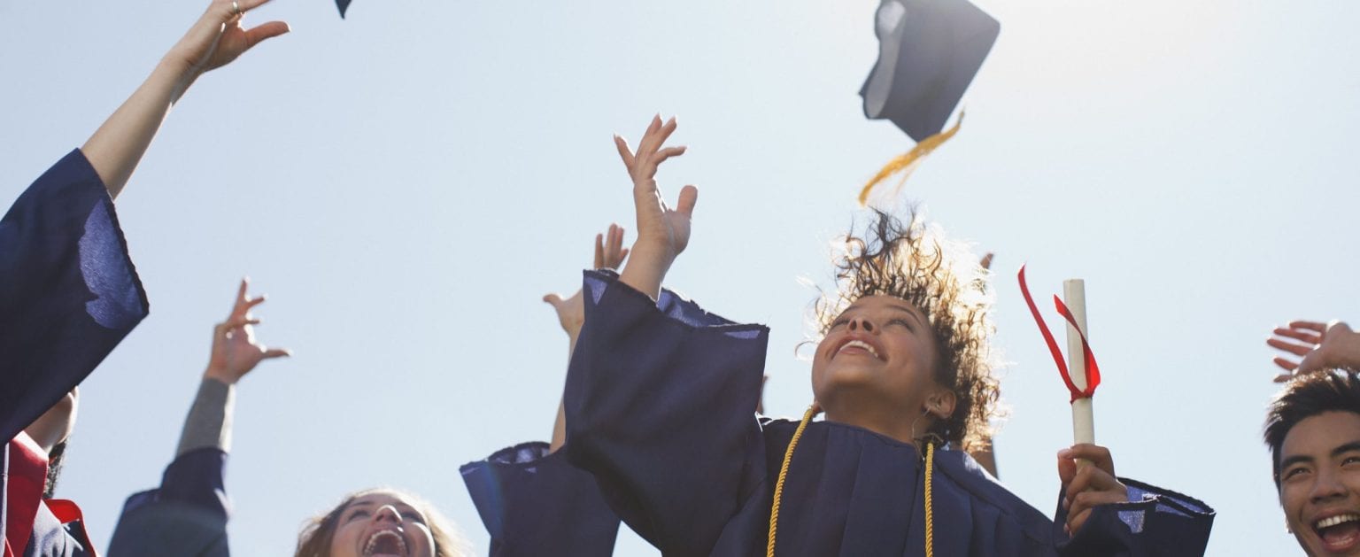 A group of recent graduates toss their graduation caps in the air in celebration.