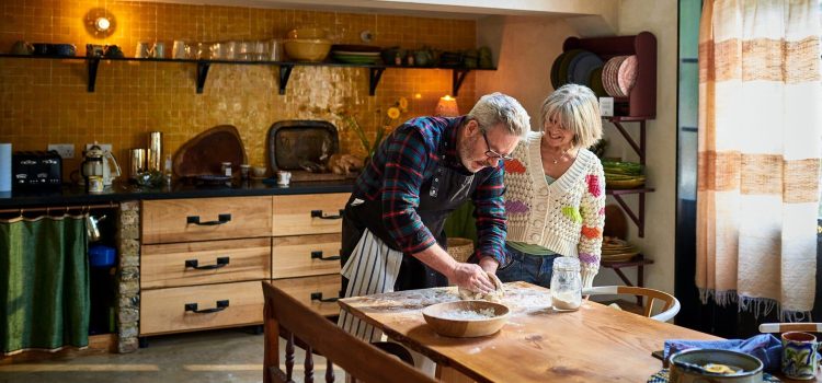 A retired couple roll out bread dough together on their dining table.