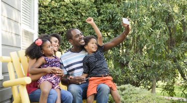 A mother and father with their son and daughter sitting on a bench outside.