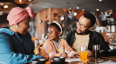 A family eats breakfast while the daughter smiles at her mother and father