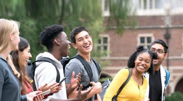 A group of college students laughing outside a campus building.