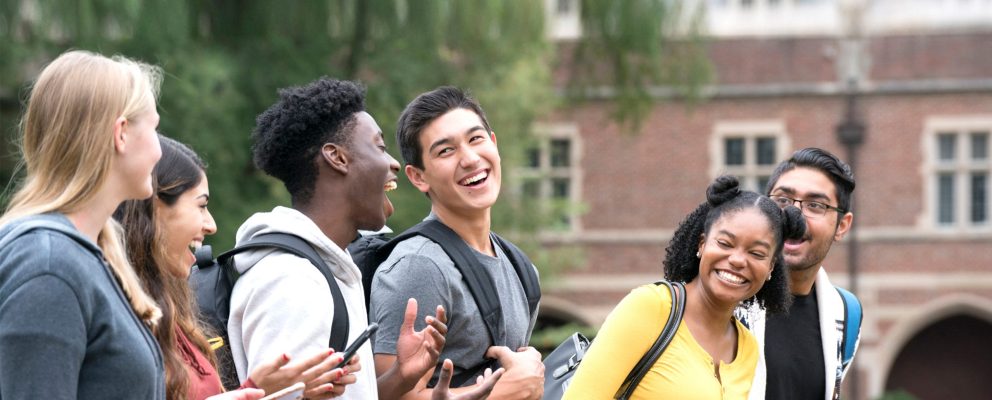 A group of college students laughing outside a campus building.