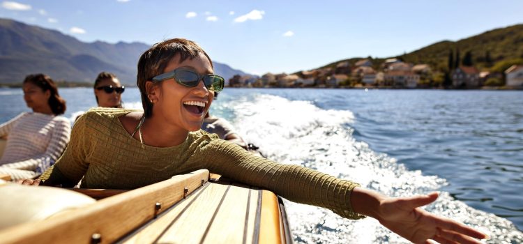 A woman on a boat with 2 others extends her hand over the water with a big smile