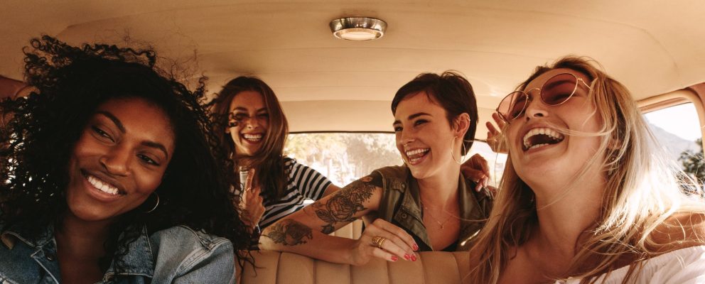 Four female friends smile and laugh during a road trip.