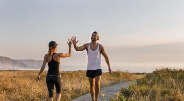 A man and a woman in workout gear high five in a field by the ocean.