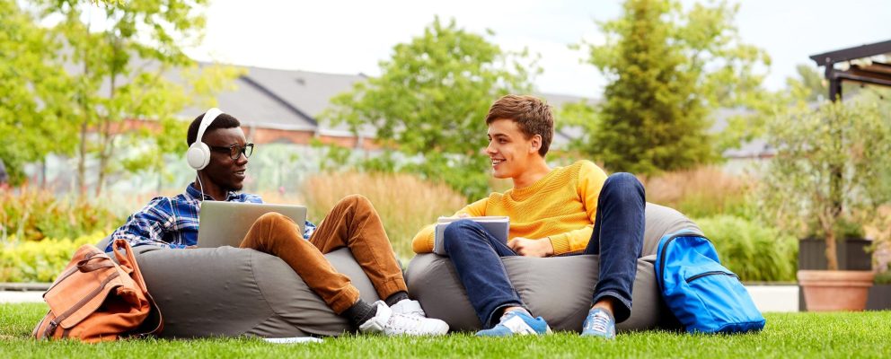 2 students lounge on bean bag chairs in the grass