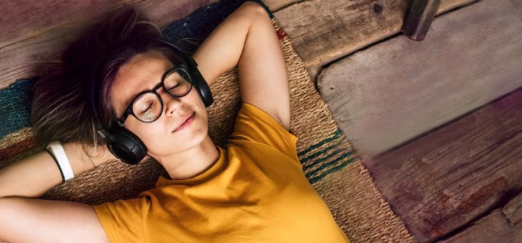 A woman with glasses relaxes with her hands behind her head and her eyes closed