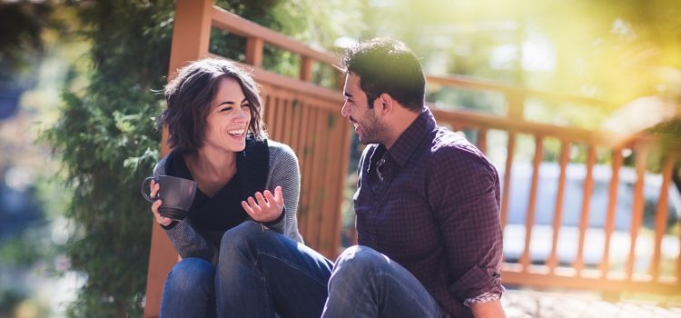 A man and a woman sit on a bench laughing.