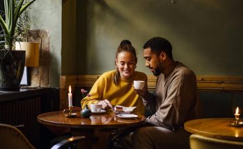 A couple at a café share a desert and drink coffee.