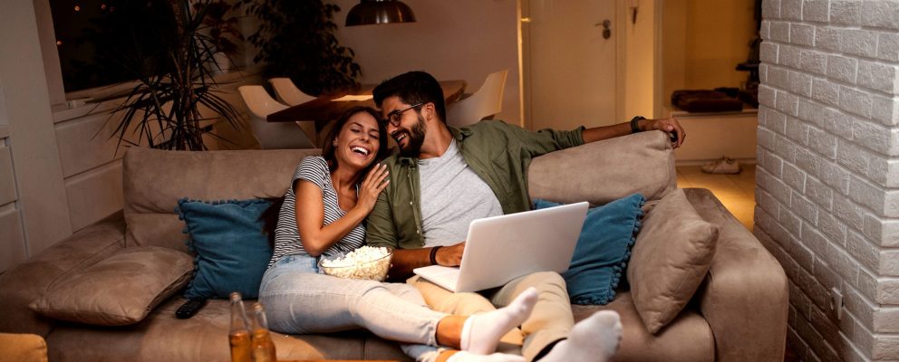 A couple relaxes on a couch with their feet up and laugh