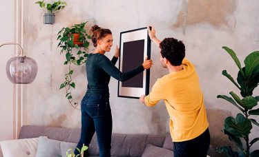 A man and woman hanging a picture frame in a living room.