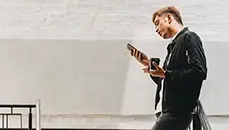A young man stands in stairwell holding paper coffee cup and scans his mobile phone.