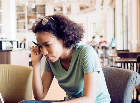 Young woman sits on a coffee shop chair working on a laptop.